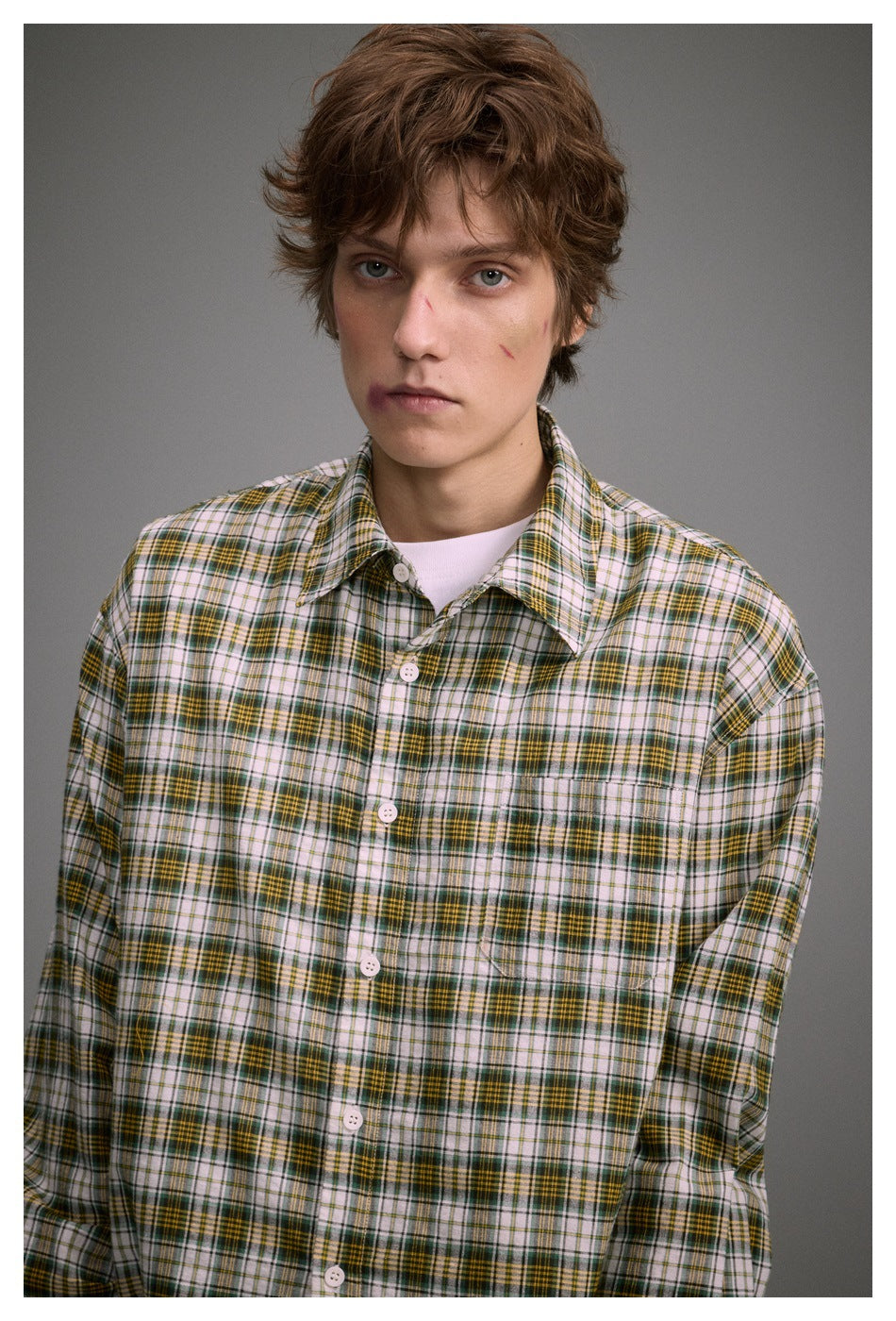 Close-up of a model wearing a yellow-green plaid button-up shirt with chest pocket over a white tee