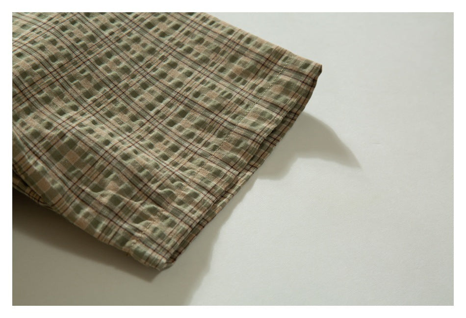 Close-up of the finished edge of olive, tan, and brown plaid fabric on a light background.