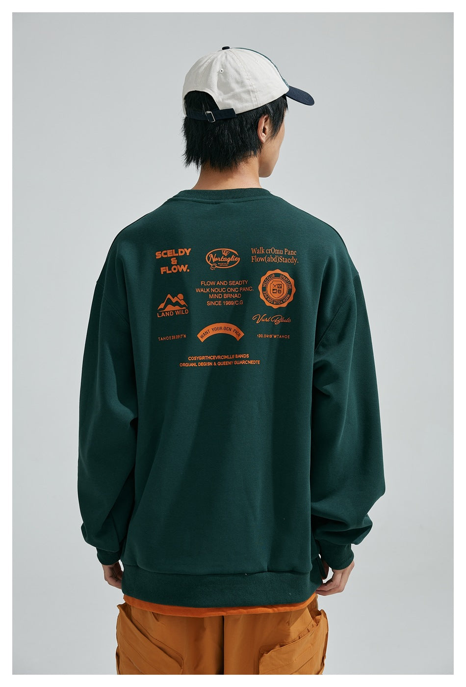 Close back view of a model in a dark green sweatshirt with large orange badge and text prints