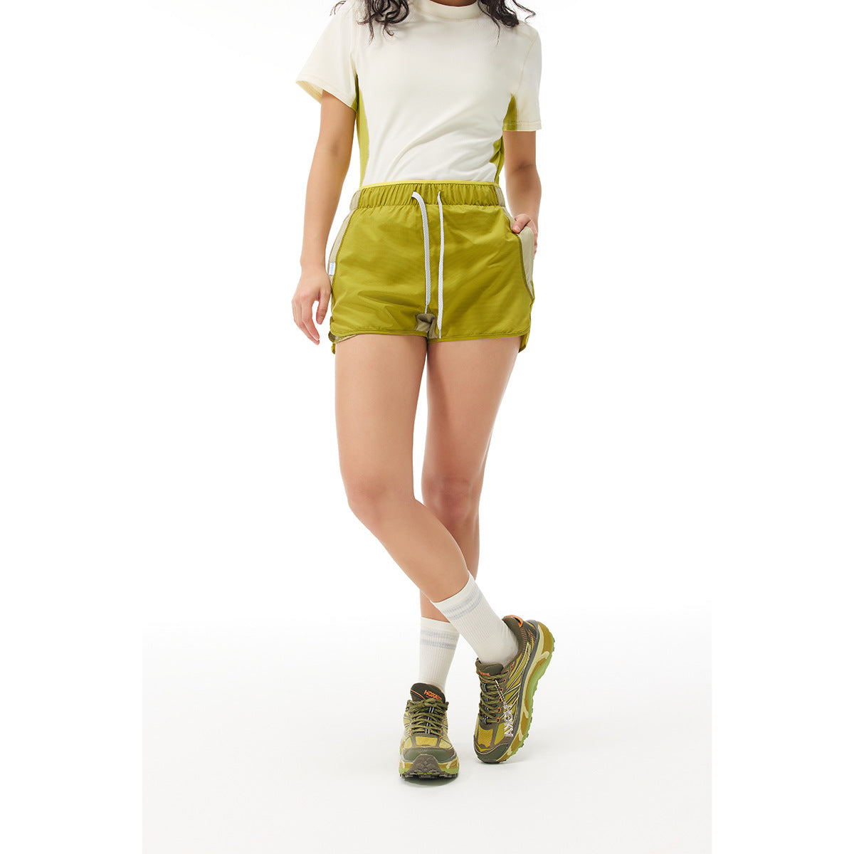 Front view of a model wearing olive-yellow running shorts with a white drawstring and light side panels.