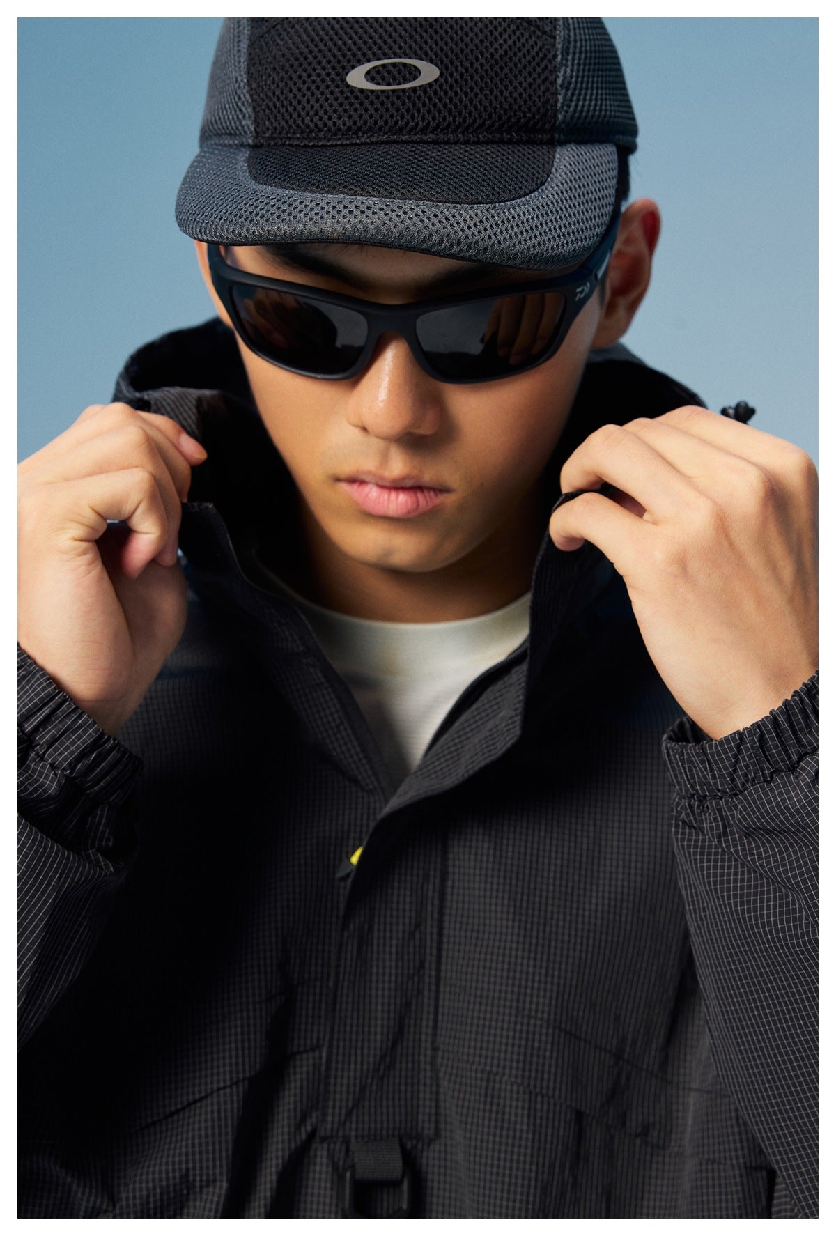 Close-up of a man holding open the collar of a black grid-textured hooded windbreaker.