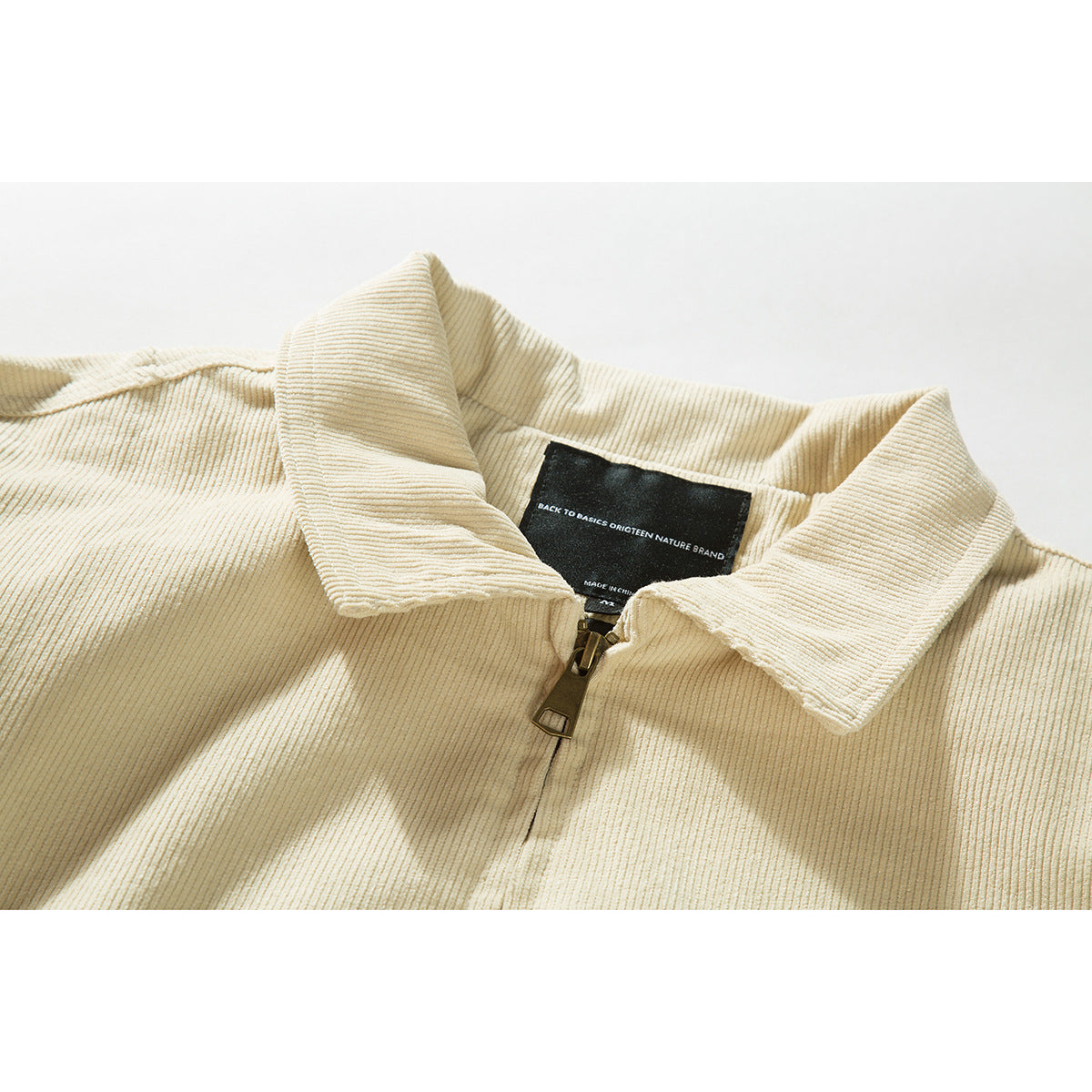 Close-up of a cream ribbed jacket collar and zipper with a black inside neck label.