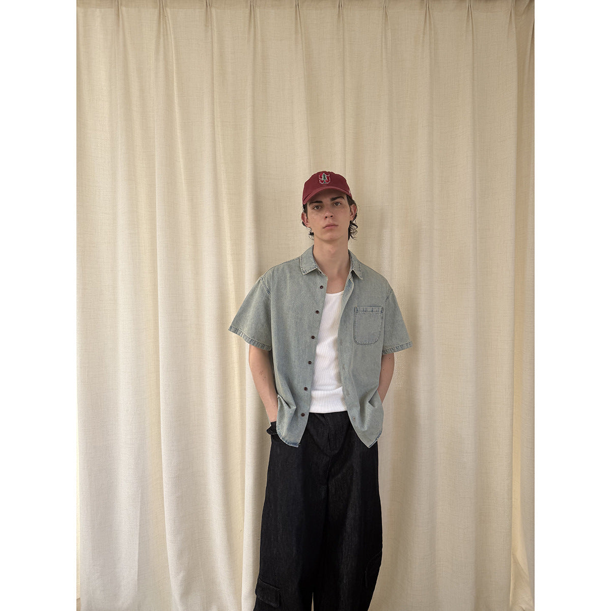 Model wearing an open light blue short-sleeve shirt over a white top with wide black trousers.