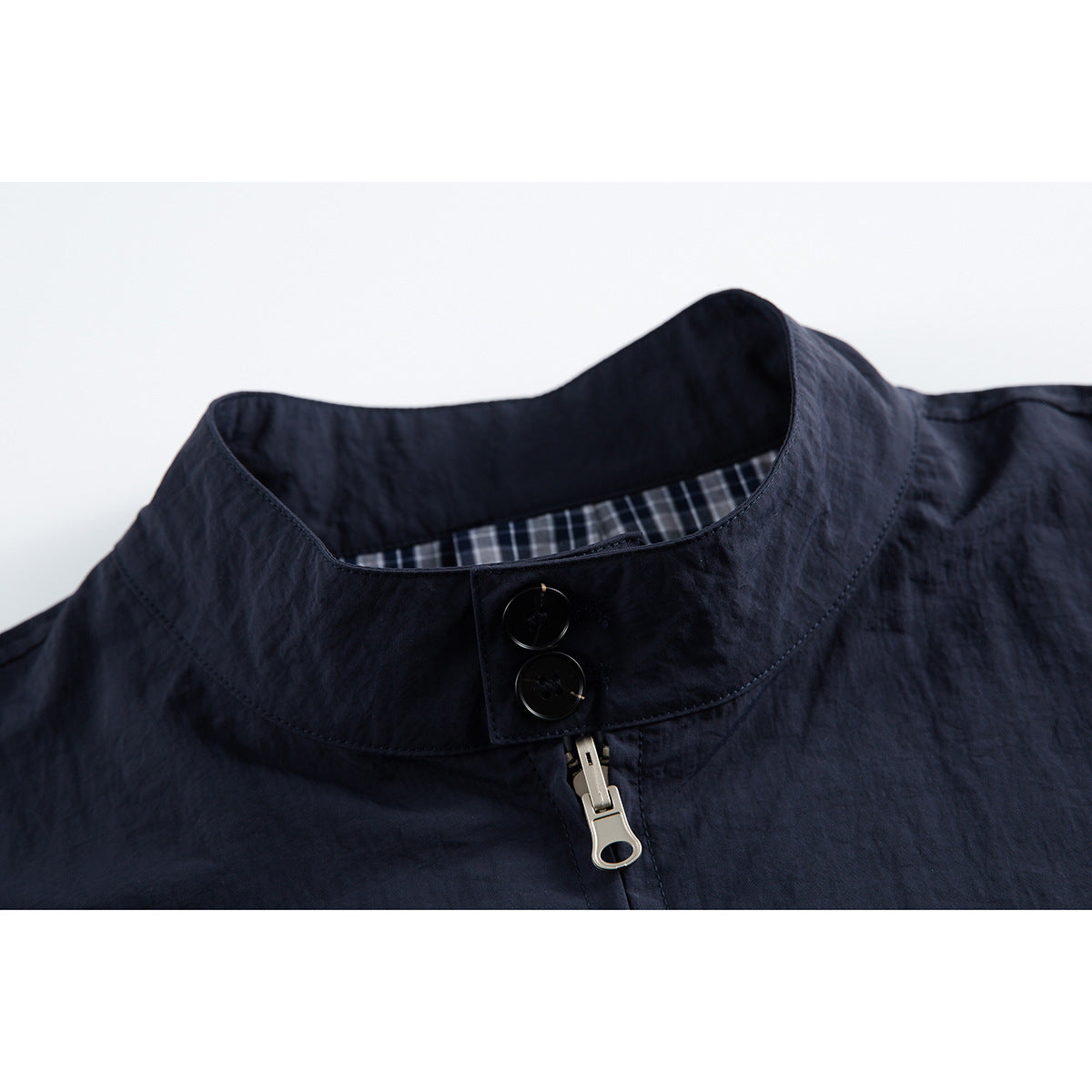 Close-up of a dark navy jacket’s stand collar, with two buttons, a metal zipper pull and checked inner lining.