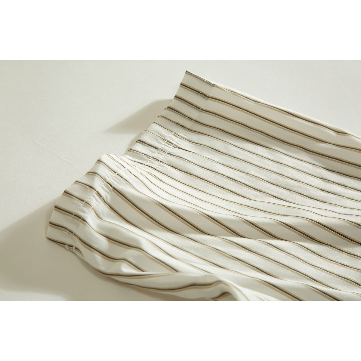 Close-up of cream fabric with thin brown and gray stripes, folded to show a stitched edge.