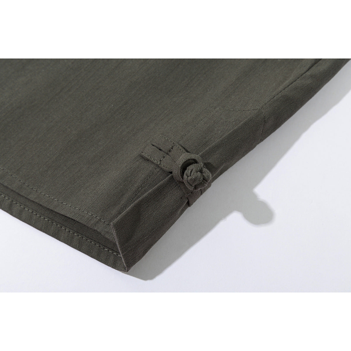 Close-up of an olive-gray shirt hem with a small fabric tie detail and visible stitching.