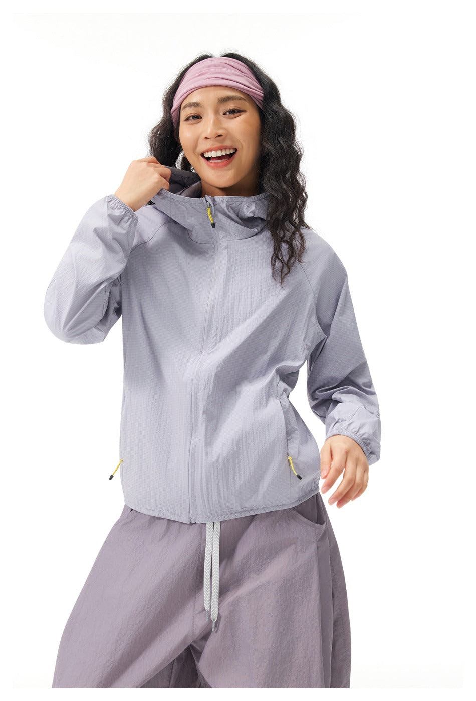 Model wearing a light gray-lavender hooded zip jacket with yellow zipper pulls and loose matching trousers.