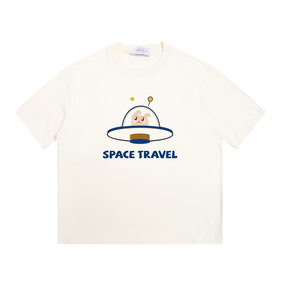 Apricot cream short-sleeve crew-neck T-shirt with a cartoon UFO creature graphic and blue 'SPACE TRAVEL' text, flat lay