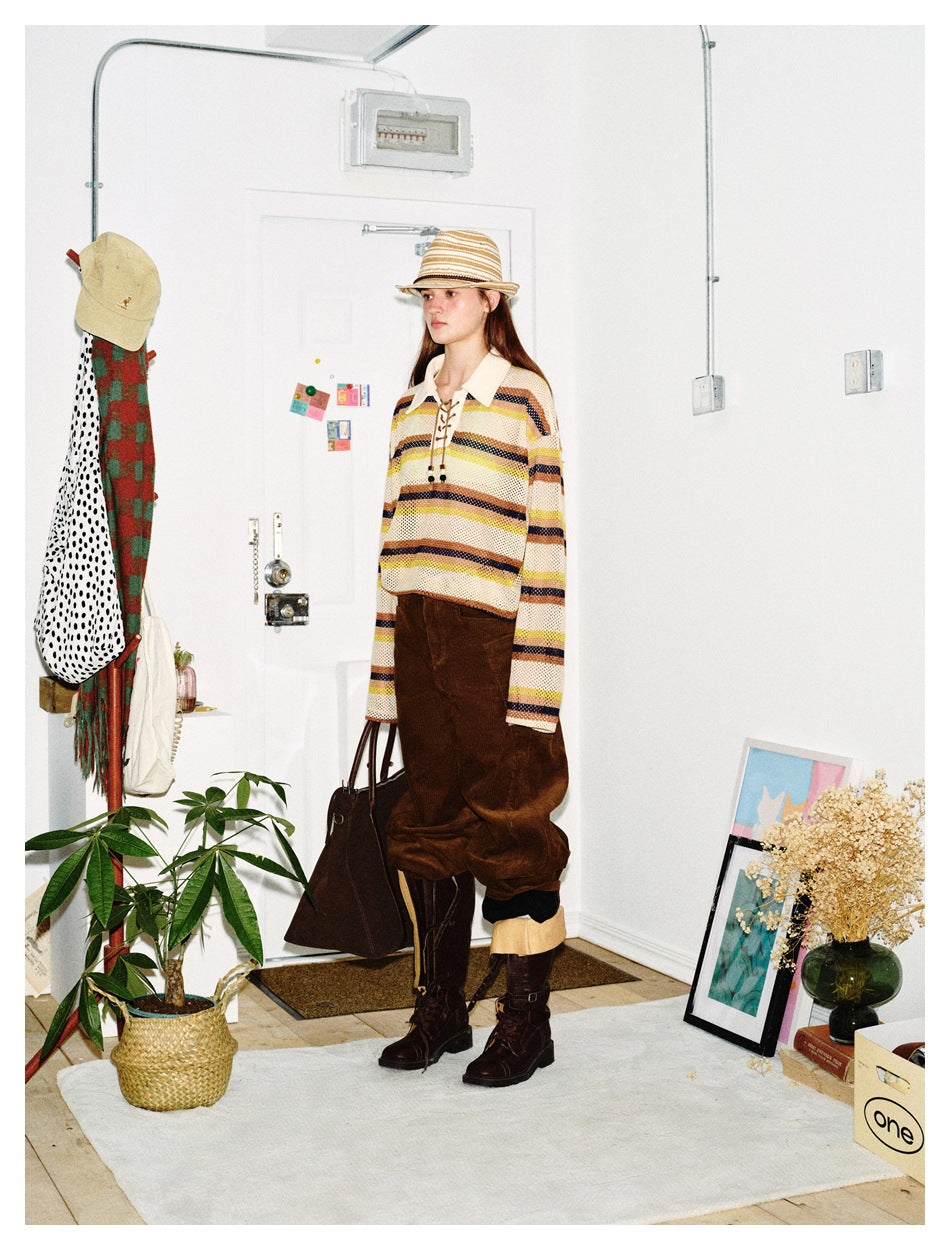 Model in a three-quarter view of the striped mesh lace-up polo top styled with brown pants, boots and a straw hat