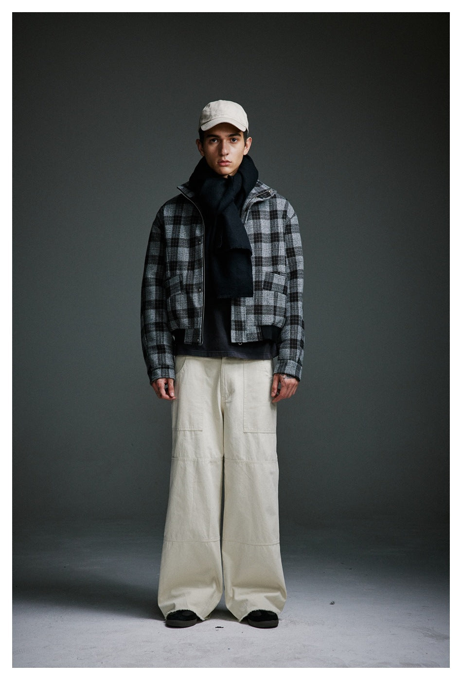 Model wearing a cropped black and gray plaid zip jacket with a black scarf, beige cap and cream wide-leg pants