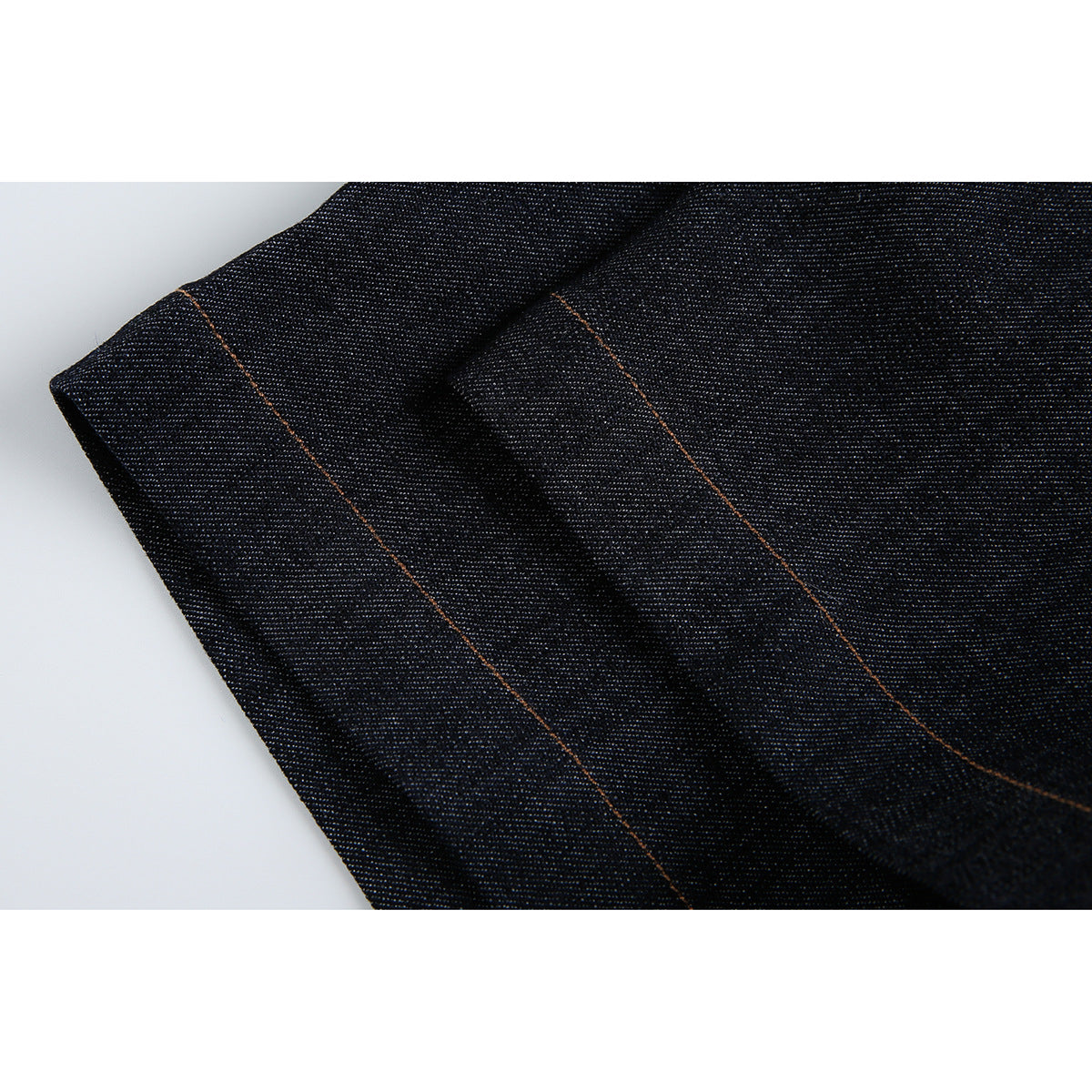 Close-up of a folded edge and orange-stitched seams on dark indigo denim.