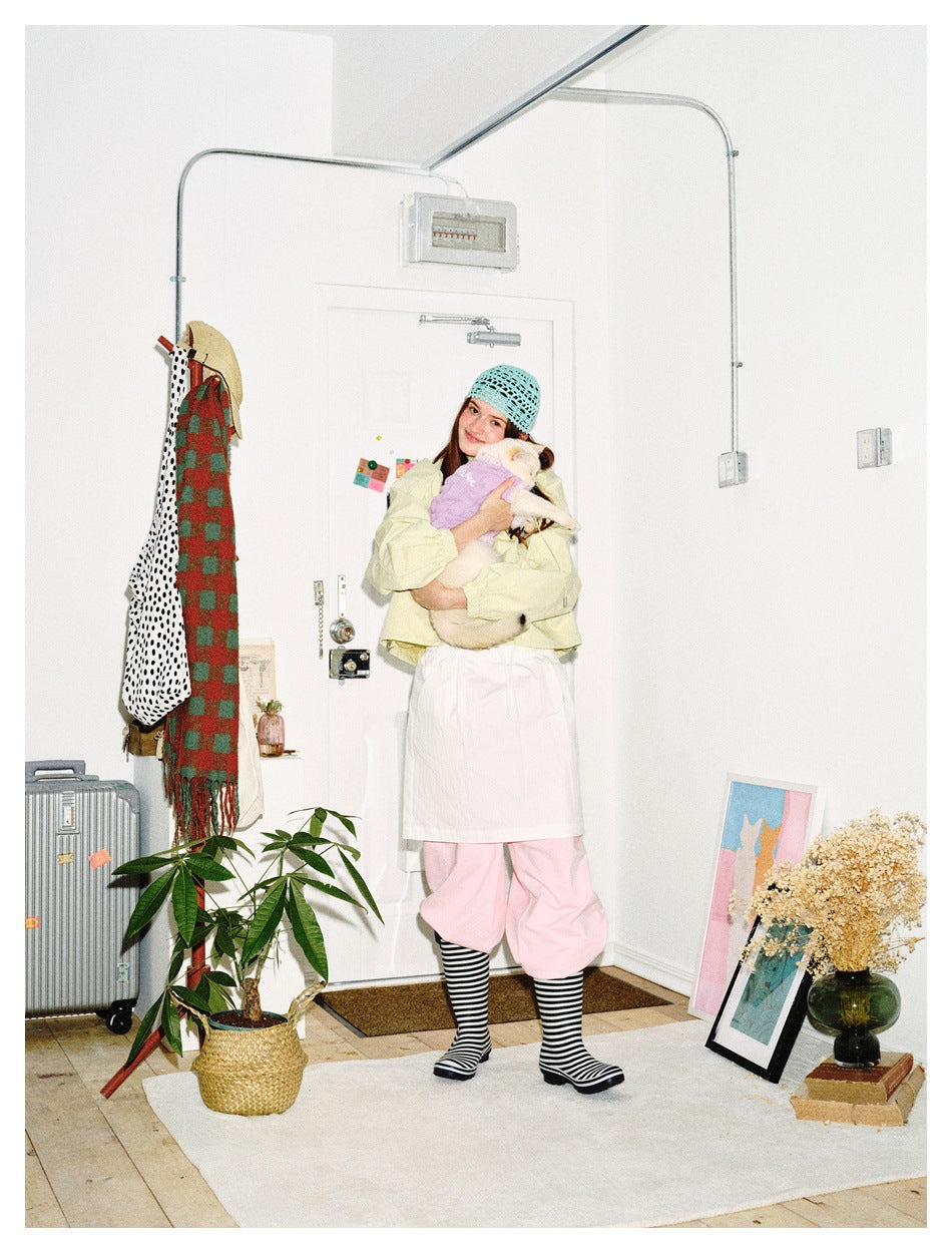 Model wearing a pale yellow cropped jacket and pink trousers, cuddling a cat in a purple sweater.