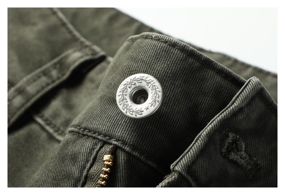 Close-up of an engraved silver waistband button and the dark olive-gray fabric.
