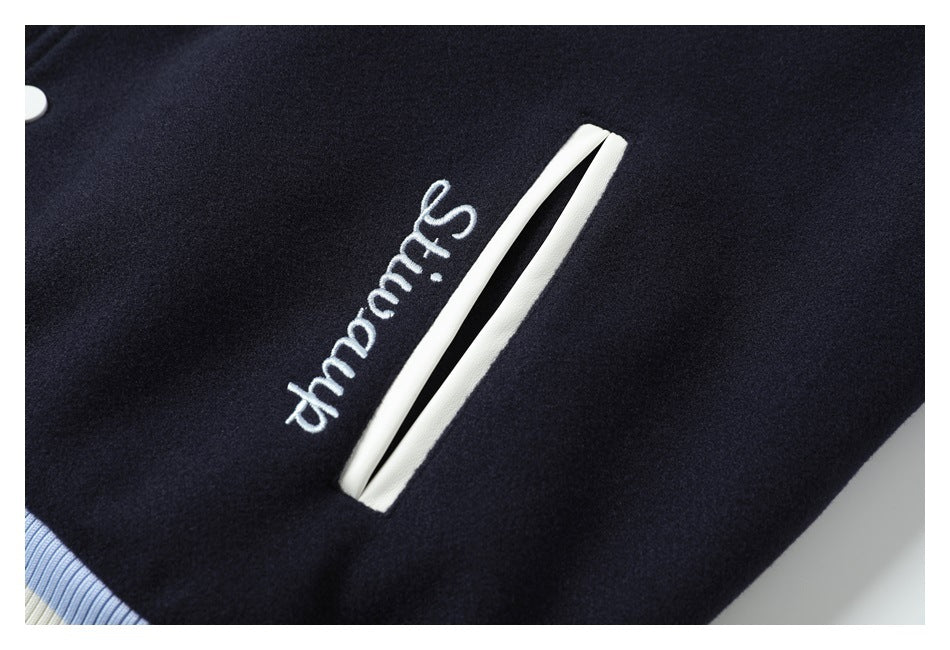 Close-up of a navy garment with white script embroidery beside a white-trimmed slit pocket and striped ribbing.