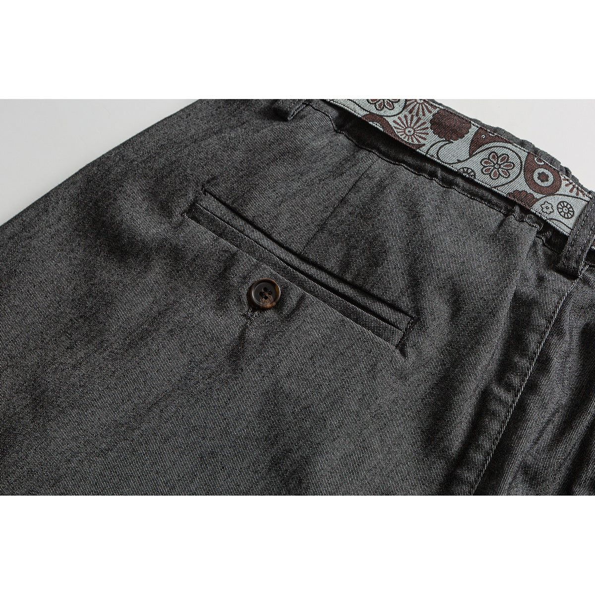 Close-up of charcoal trousers’ back pocket and button, with a patterned strip visible at the waistband.