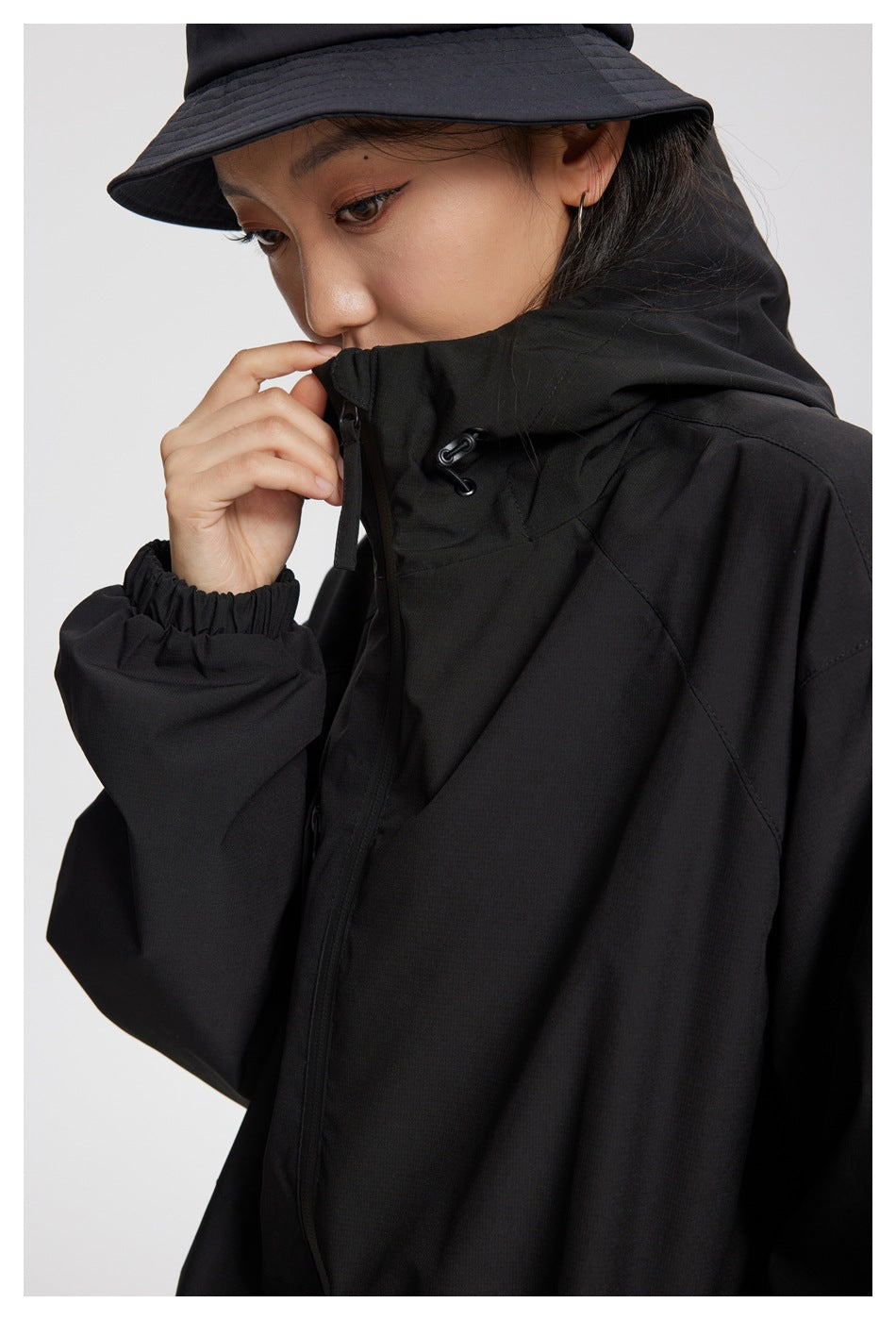 Close-up of a black jacket's raised hood, adjustable drawcord, zipper, and elastic cuff.