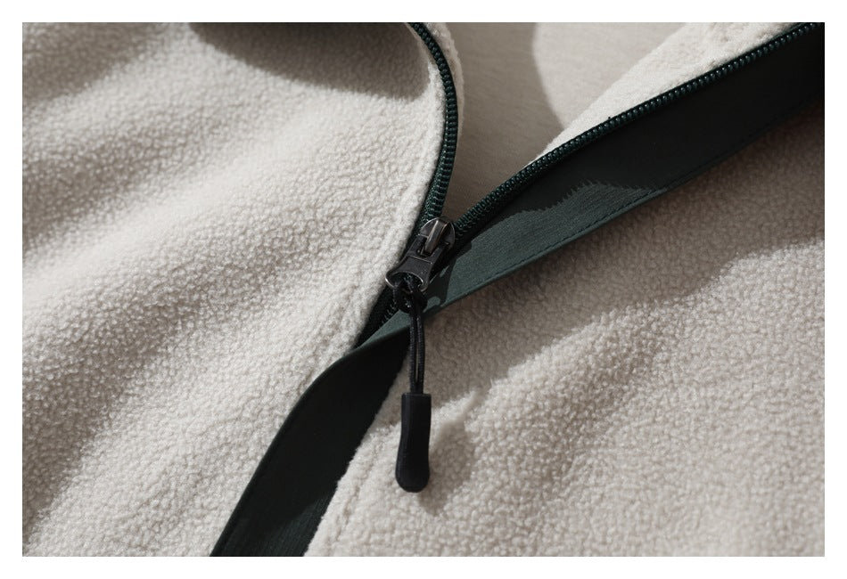 Macro view of the jacket’s dark zipper, pull cord, and green trim against cream sherpa fabric.