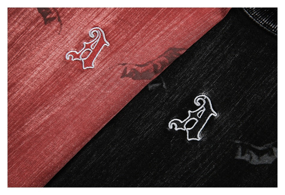 Close-up of muted red and black T-shirts showing matching white embroidered chest emblems and dark graphics.