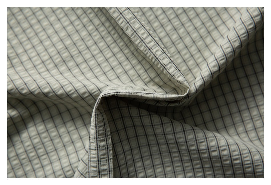 Close-up of softly folded light gray checked shirt fabric with a finished edge.