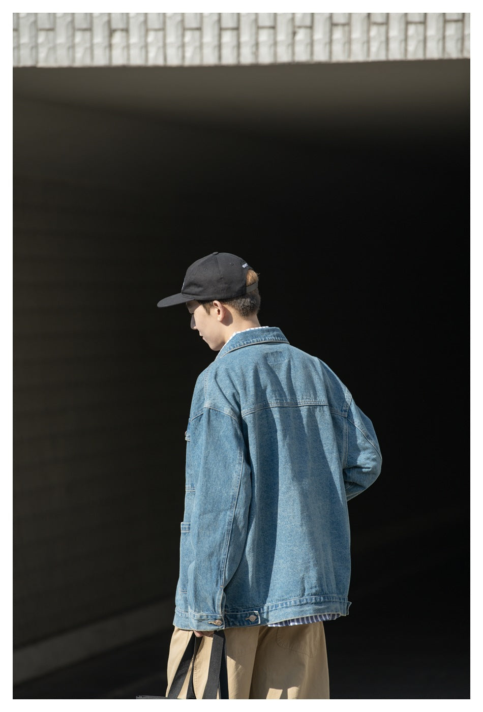 Back view of a model wearing an oversized blue denim jacket with a horizontal yoke and buttoned cuffs.