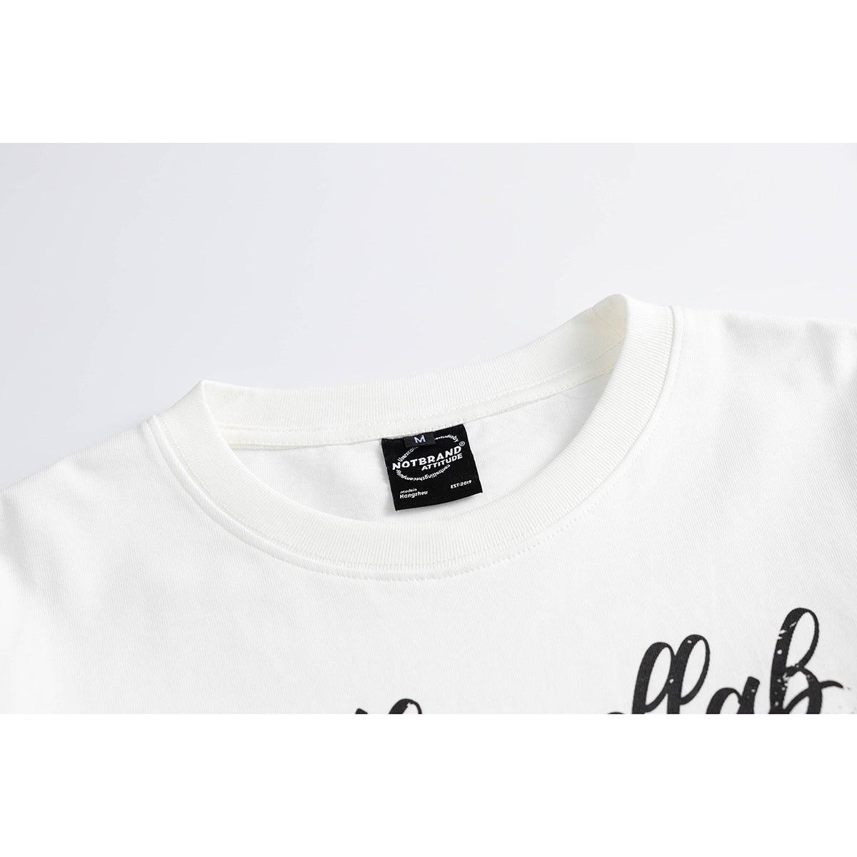 Close-up of a white long-sleeve shirt's ribbed crew neck, black neck label and partial black chest lettering.