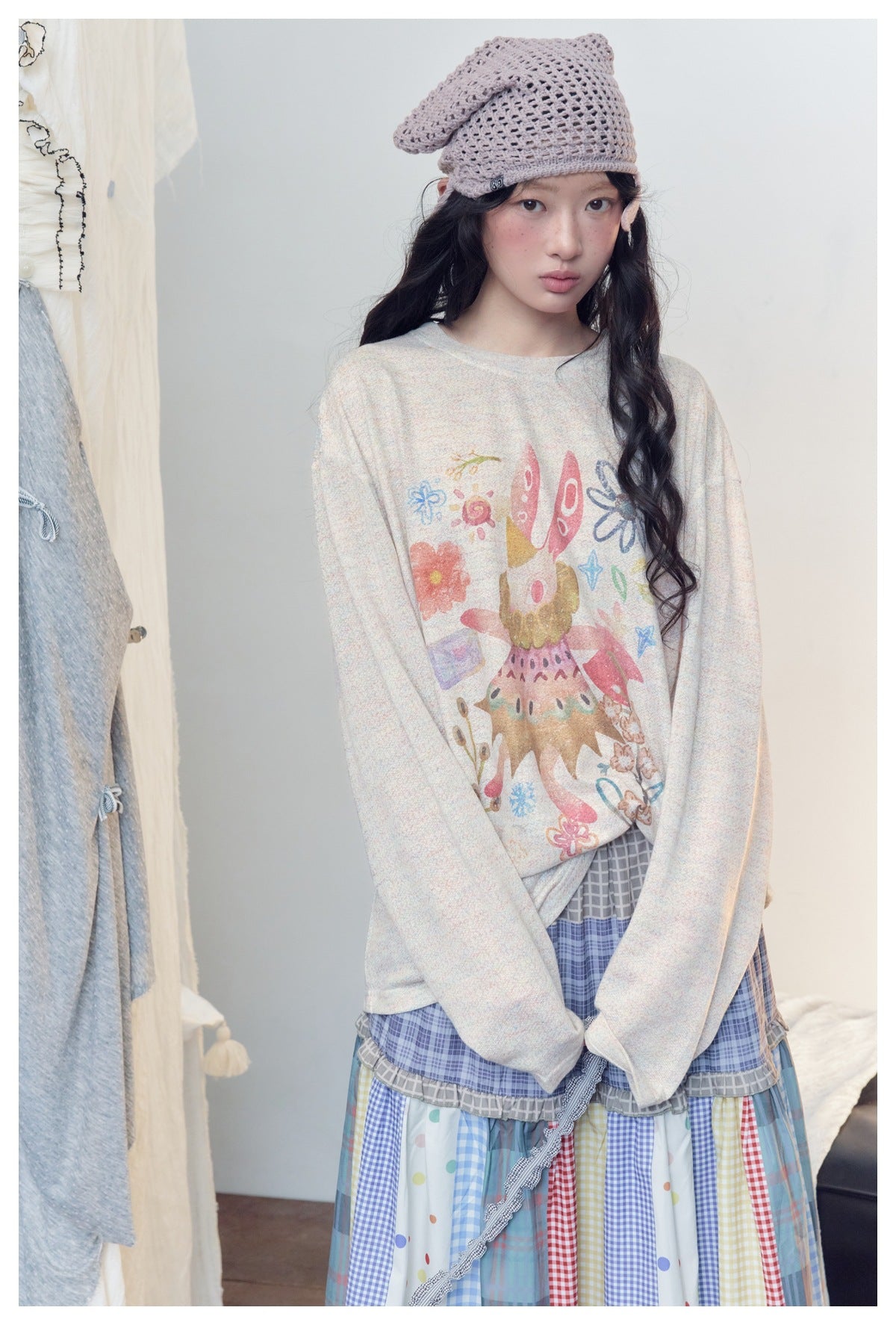 Close-up of a model wearing the cream long-sleeve top with a rabbit and flower print, with a knit headscarf and plaid skirt