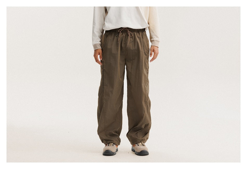 Front view of a model wearing loose olive-brown drawstring pants with gathered ankle cuffs.