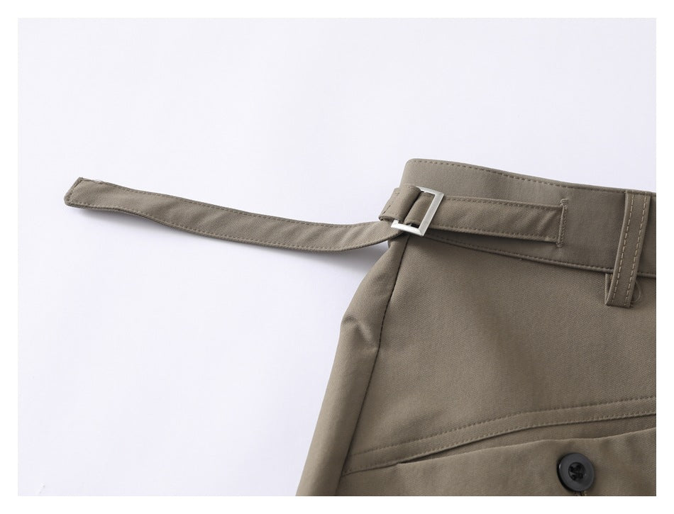 Close-up of taupe trousers showing a long waist tie, rectangular buckle and belt loops.