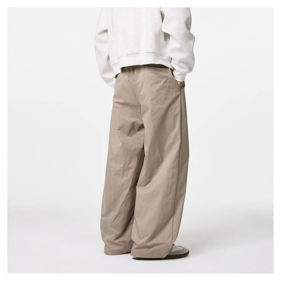 Rear view of a model wearing loose taupe trousers with wide legs and back pockets.