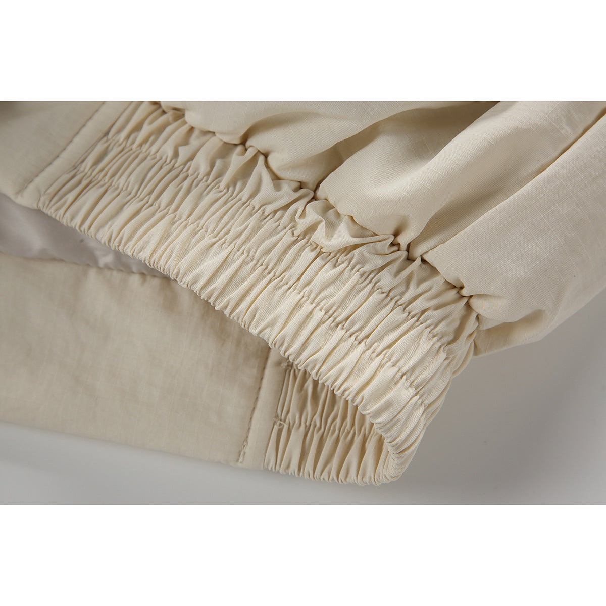 Close-up of the cream jacket's gathered elastic hem and stitched seams.