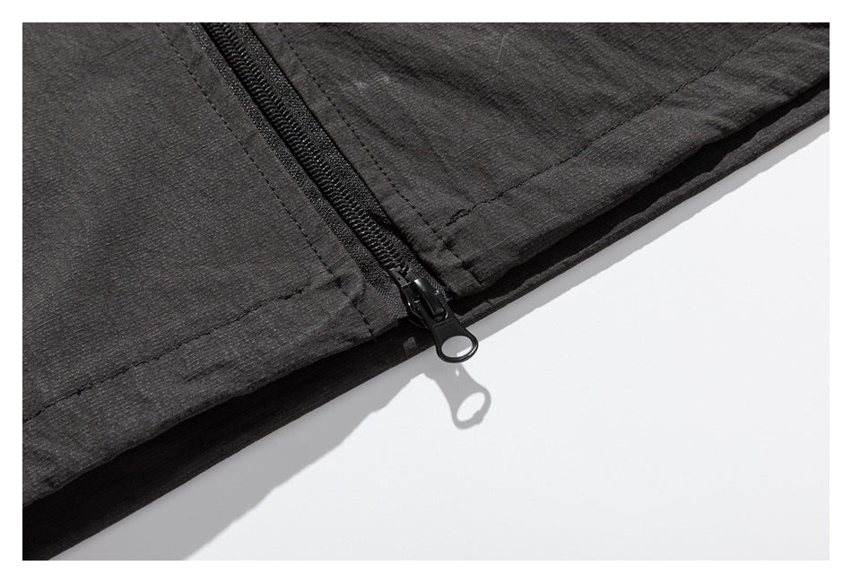 Close-up of a black zipper with a ring pull at the hem of a dark charcoal garment.