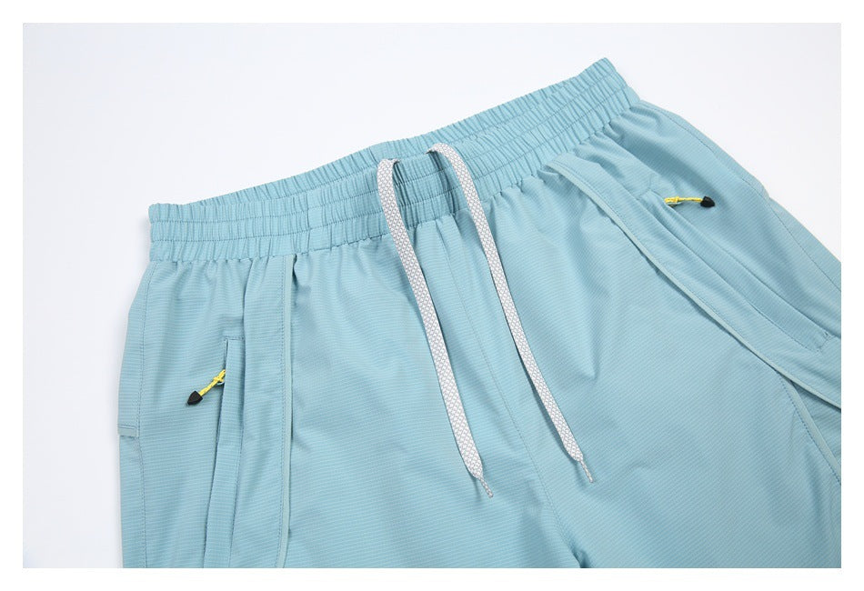 Close-up of pale blue shorts showing the elastic waistband, white drawstring, and zip pockets with yellow pulls.