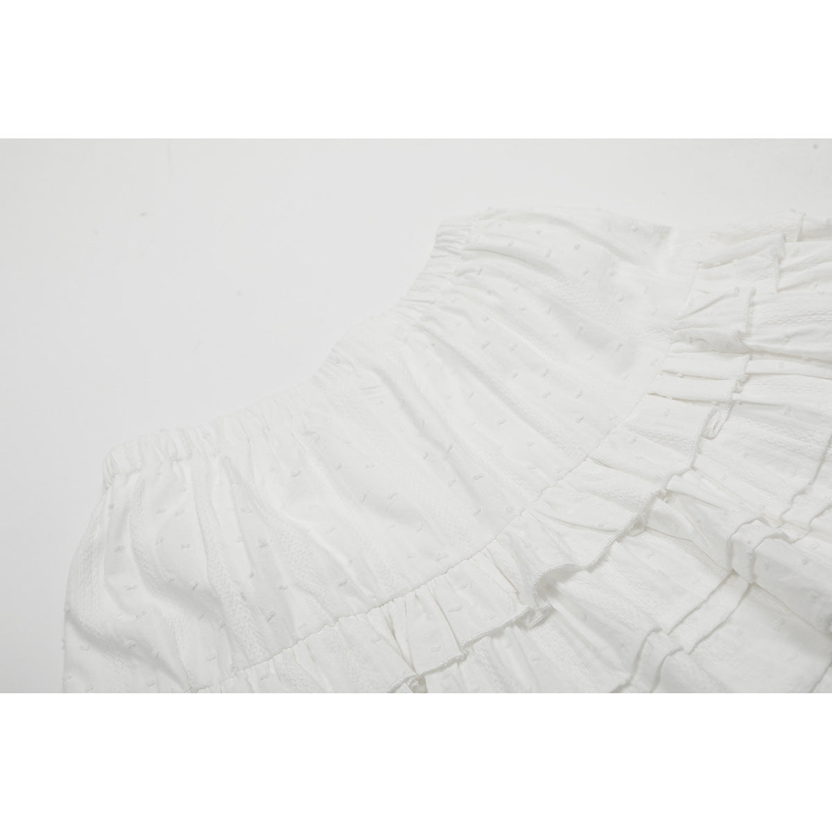 Close-up of the gathered elastic waistband and textured fabric on a white tiered skirt.