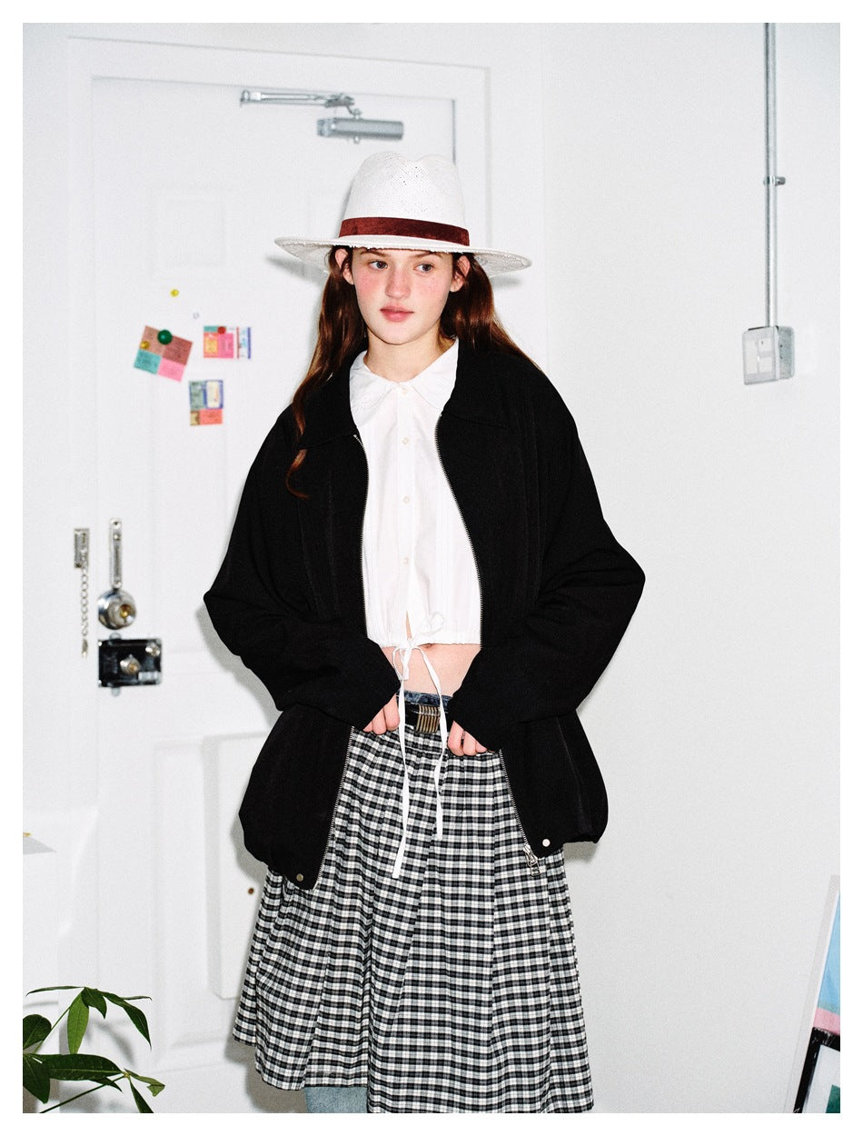 Model wearing a black collared zip jacket over a white blouse and gingham skirt.