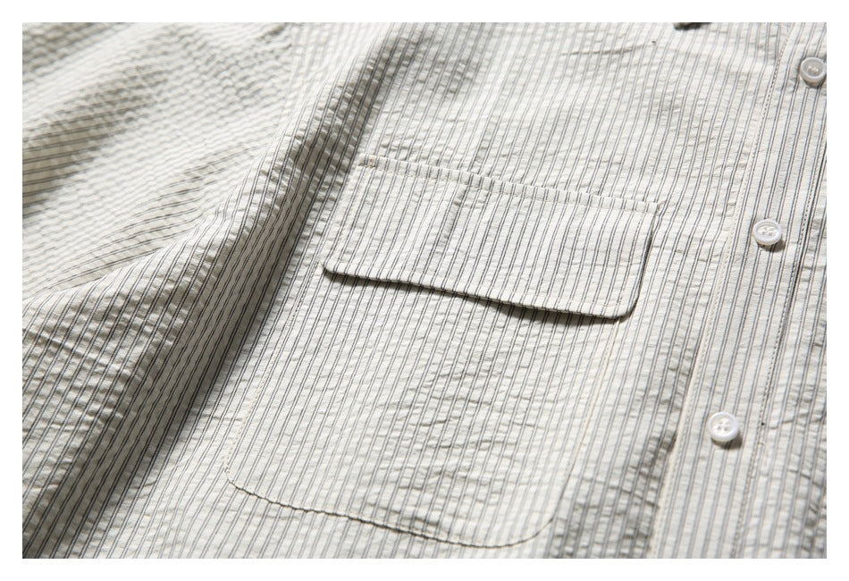 Close-up of a flap chest pocket, white buttons and fine dark stripes on the cream shirt.