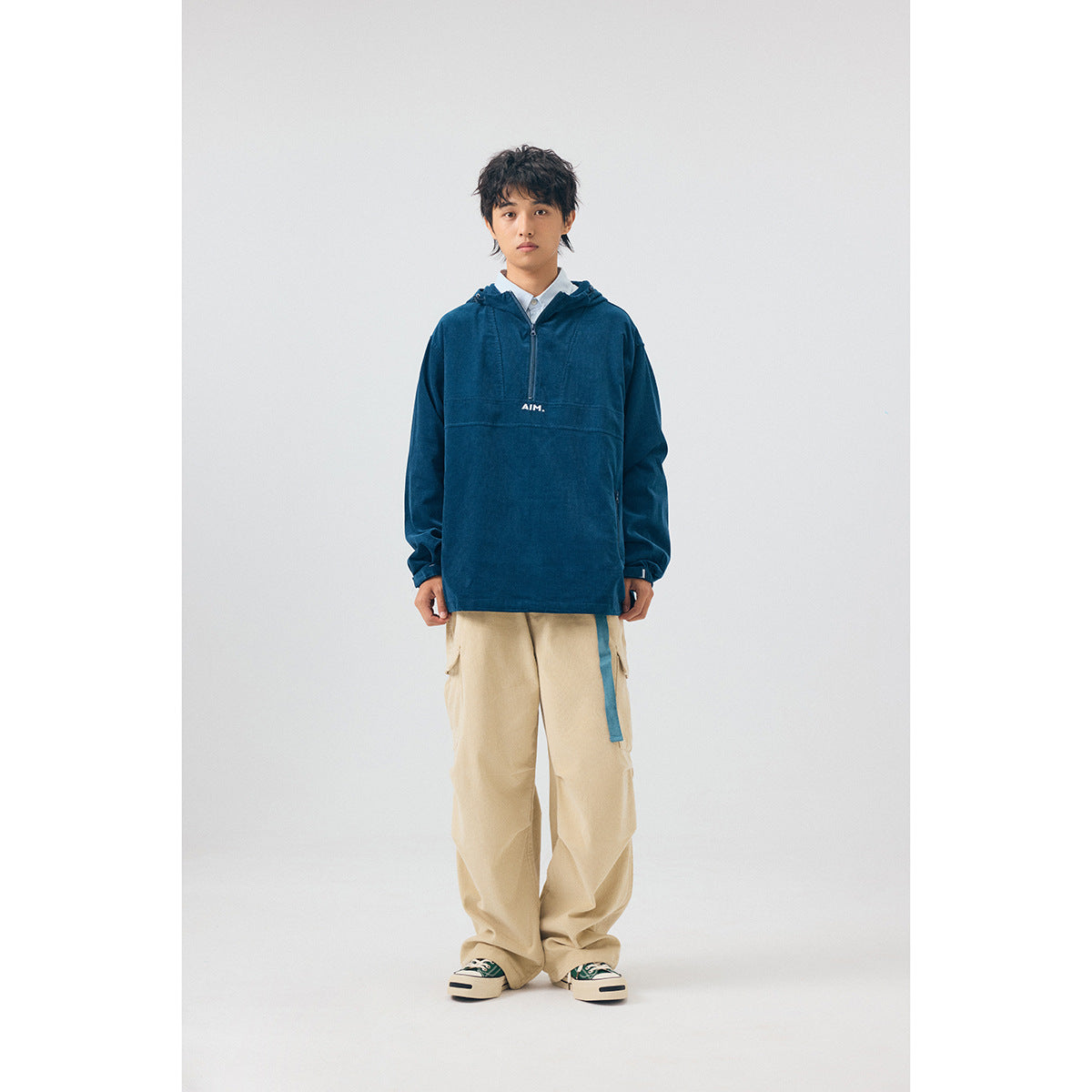 Model wearing a navy hooded pullover with a short zip and AIM chest print, paired with beige cargo pants.