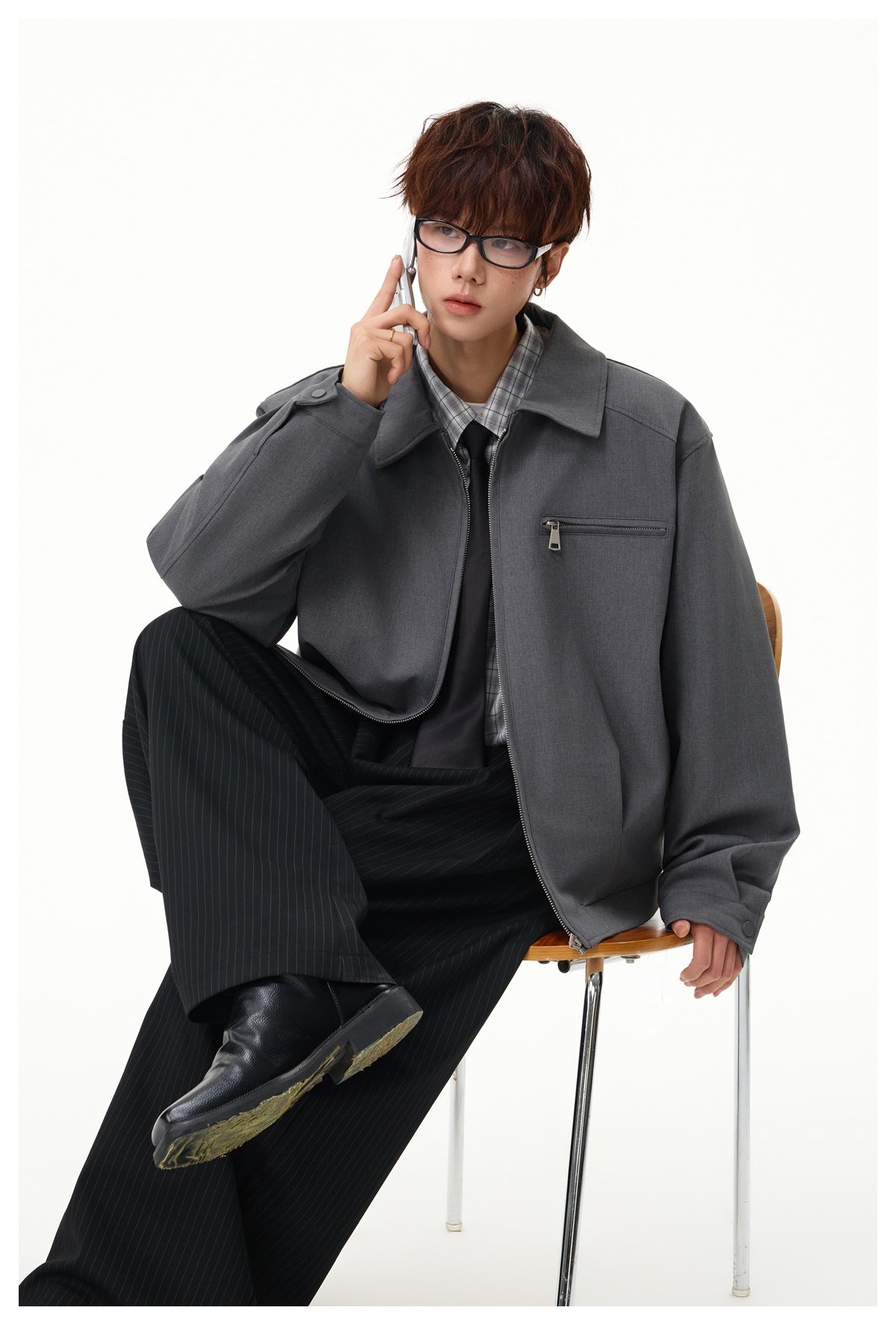 Seated model wearing a charcoal zip jacket with a chest zip pocket, plaid shirt, and black tie.