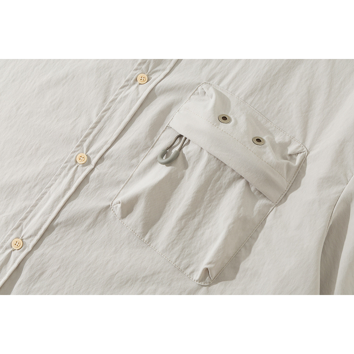 Close-up of an off-white shirt chest pocket with a buttoned flap, metal eyelets, and a small loop.