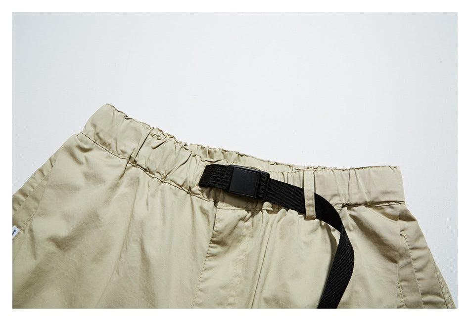 Close-up of beige shorts showing the elastic waistband and black webbing belt with buckle.