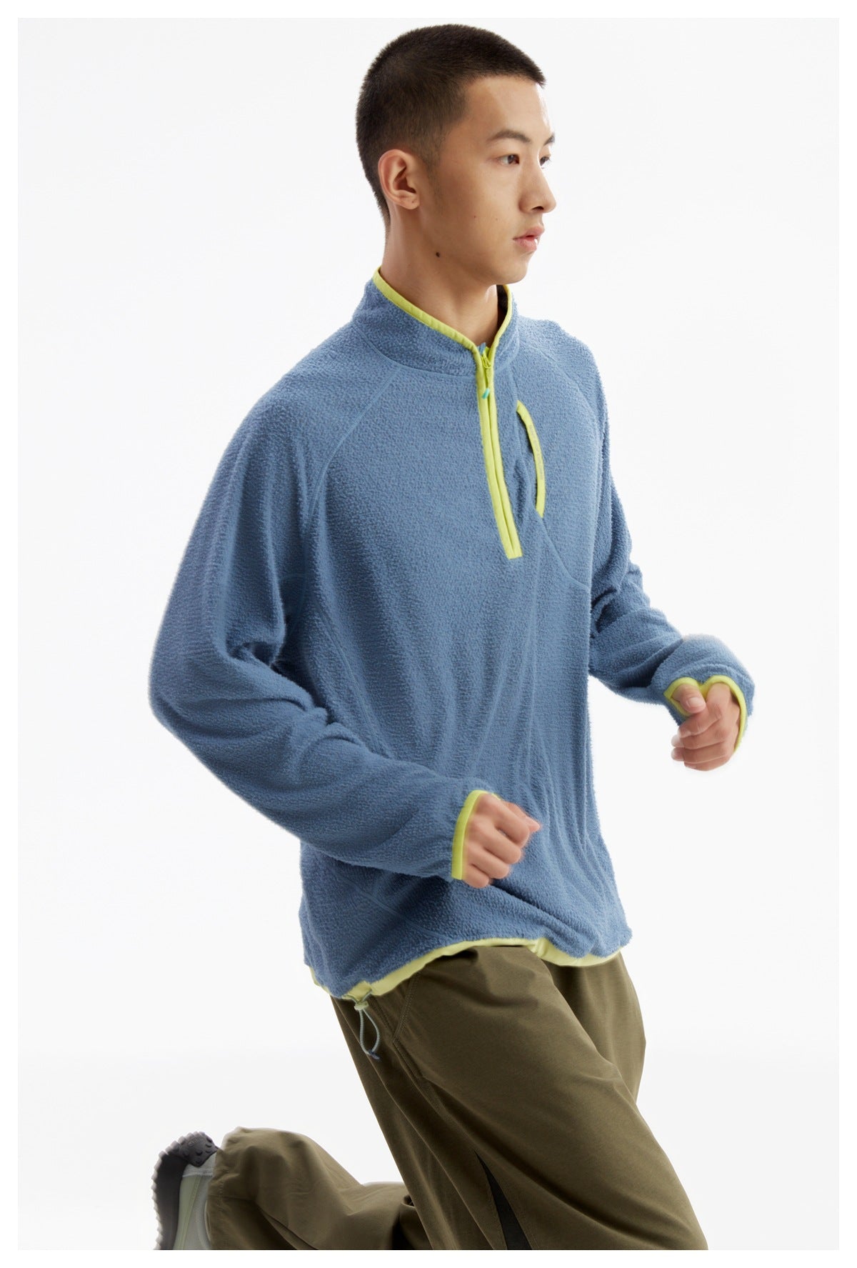 Model wearing a blue textured quarter-zip pullover with lime trim and olive trousers, shown from the front at an angle.