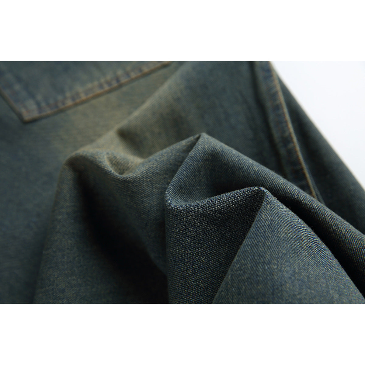 Close-up of dark indigo denim gathered to show its diagonal weave and orange-stitched seam.