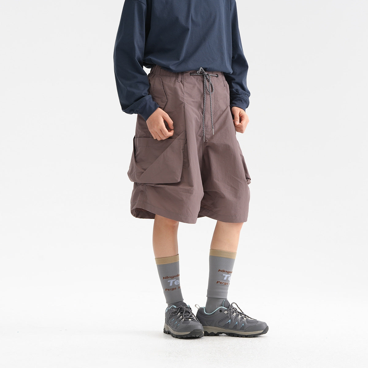 Cropped model wearing mauve-gray wide cargo shorts with a drawstring waist and large side pockets.