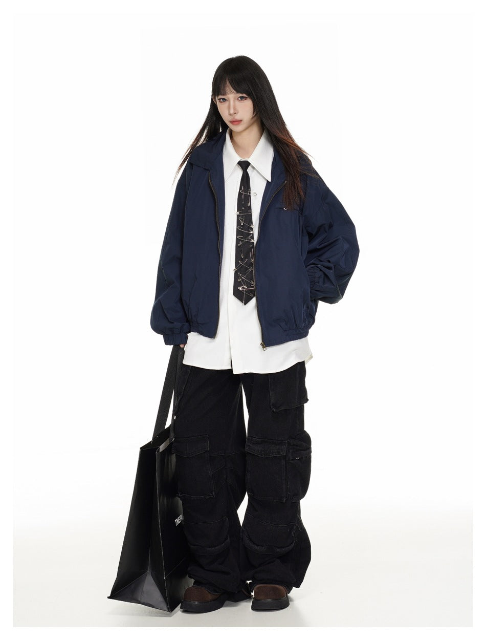 Model wearing a navy zip jacket over a white shirt and black tie, with black cargo pants and brown shoes.
