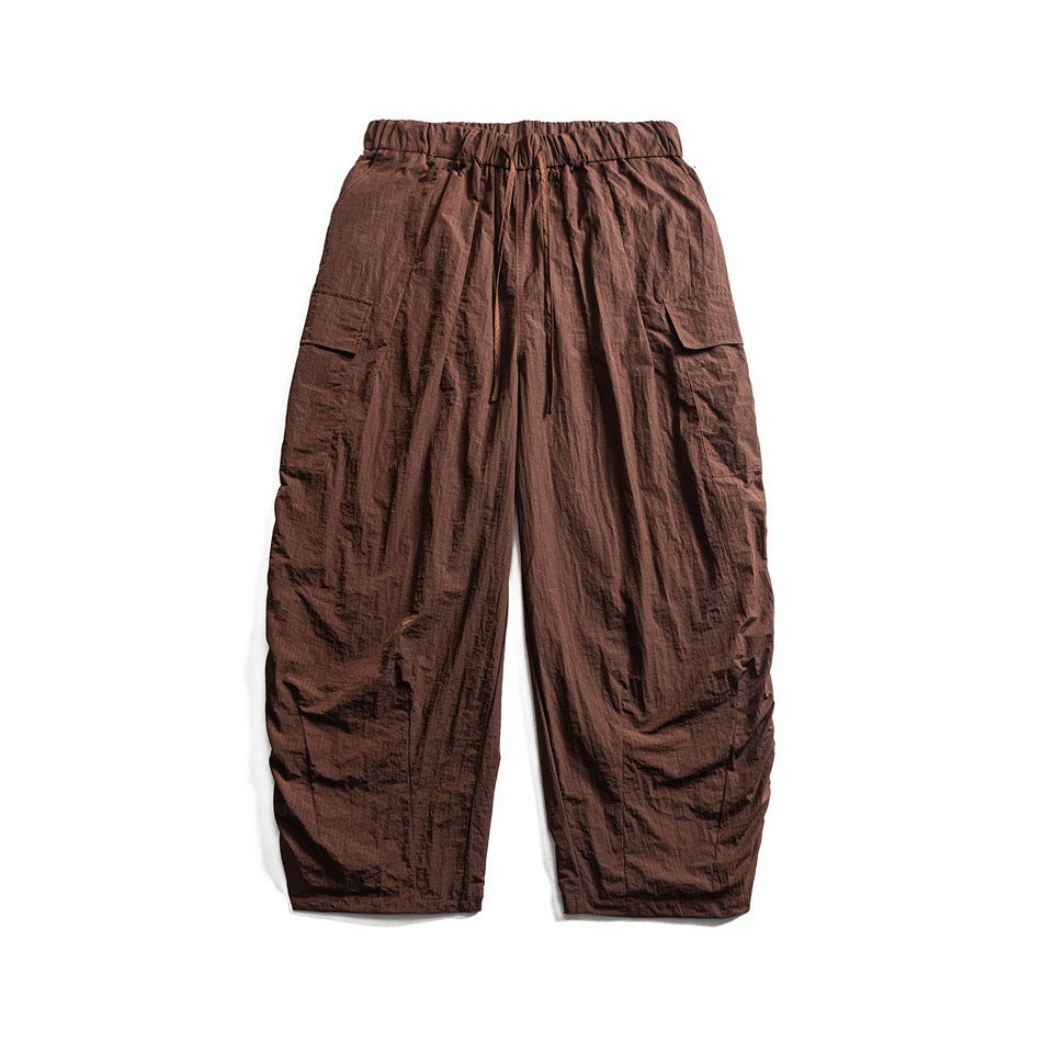 Brown wide-leg cargo pants with elastic drawstring waist and side flap pockets, flat lay on white background