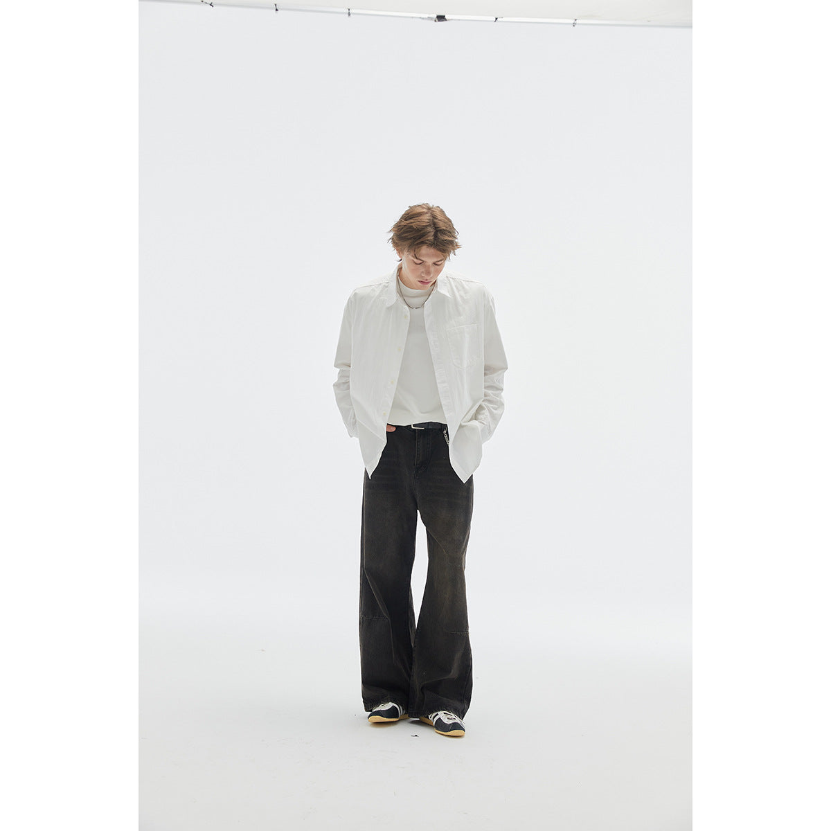 Model wearing a white button-front shirt with a chest pocket over a white tee and loose black jeans.