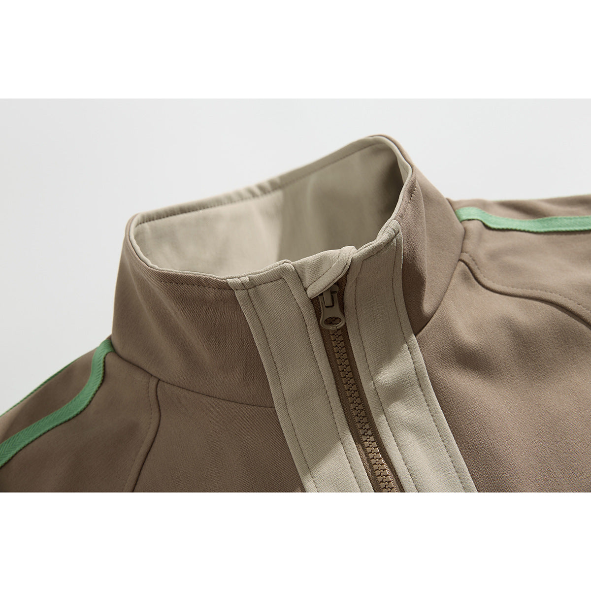 Close-up of a taupe jacket’s raised collar, beige zipper placket, and mint-green shoulder piping.