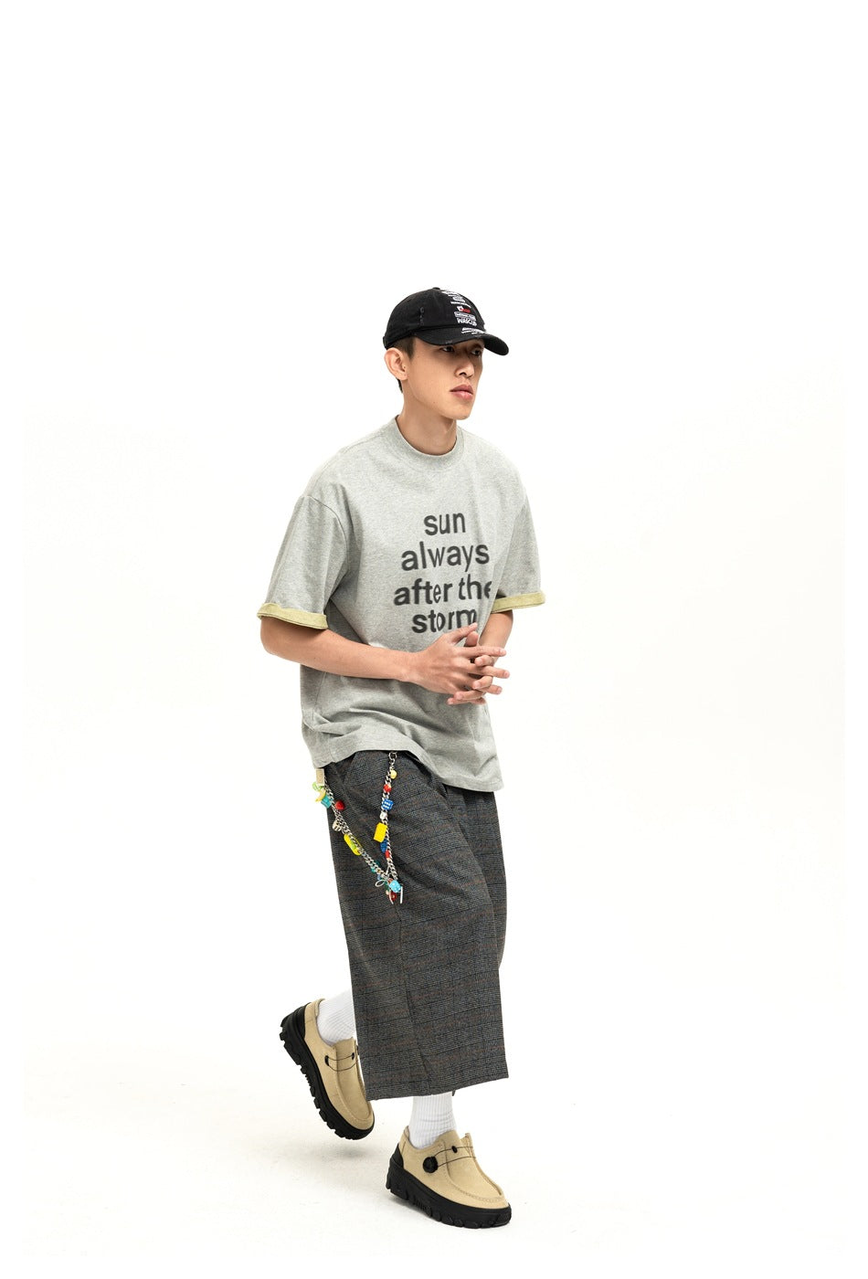 A model wears a gray T-shirt with the black slogan “sun always after the storm” and pale yellow sleeve cuffs.
