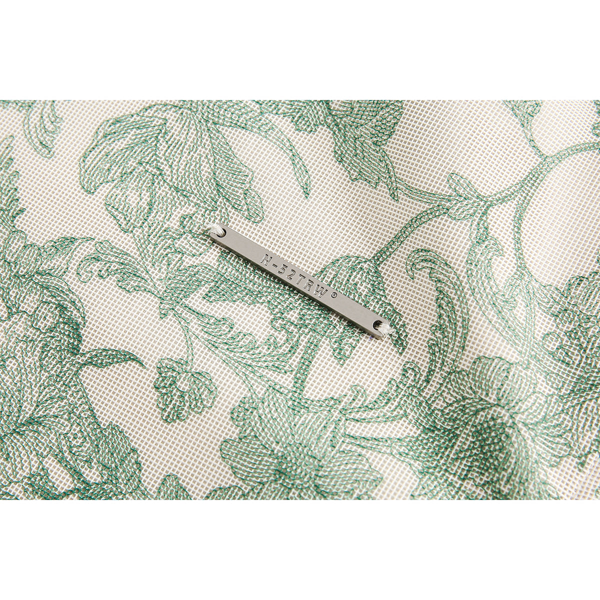 Close-up of green floral-patterned cream fabric with a small metal brand plate.
