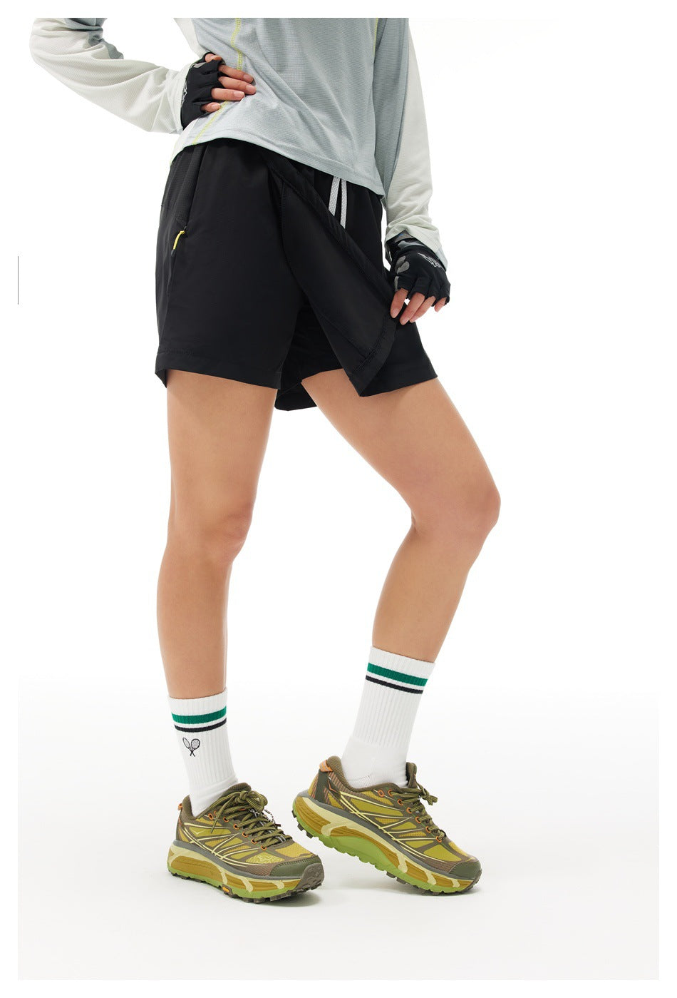 A model lifts the front overlay of a black athletic skort, showing the shorts underneath.