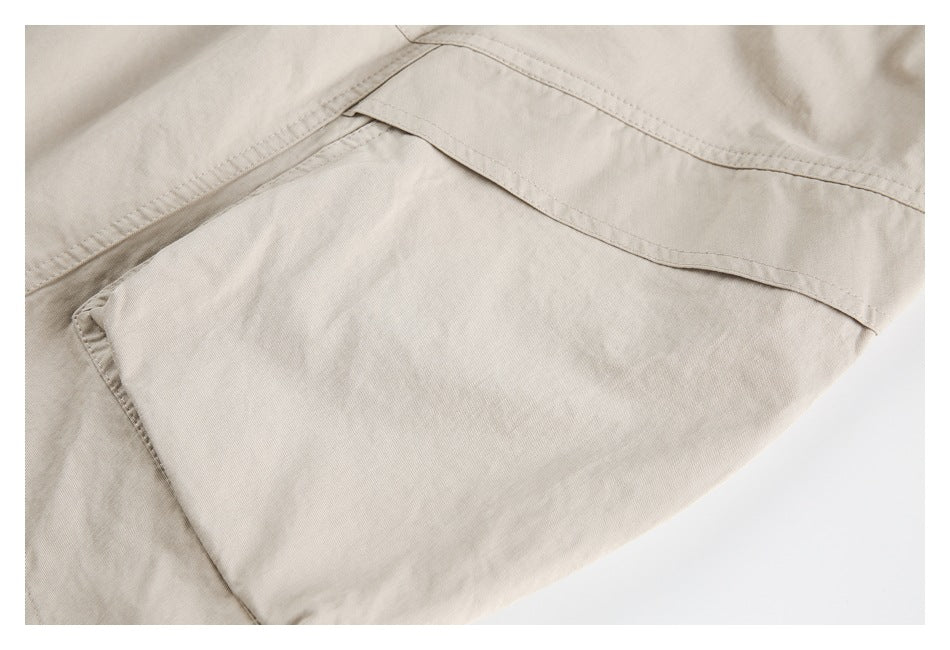 Close-up of a beige garment's stitched cargo pocket and overlapping fabric panels.
